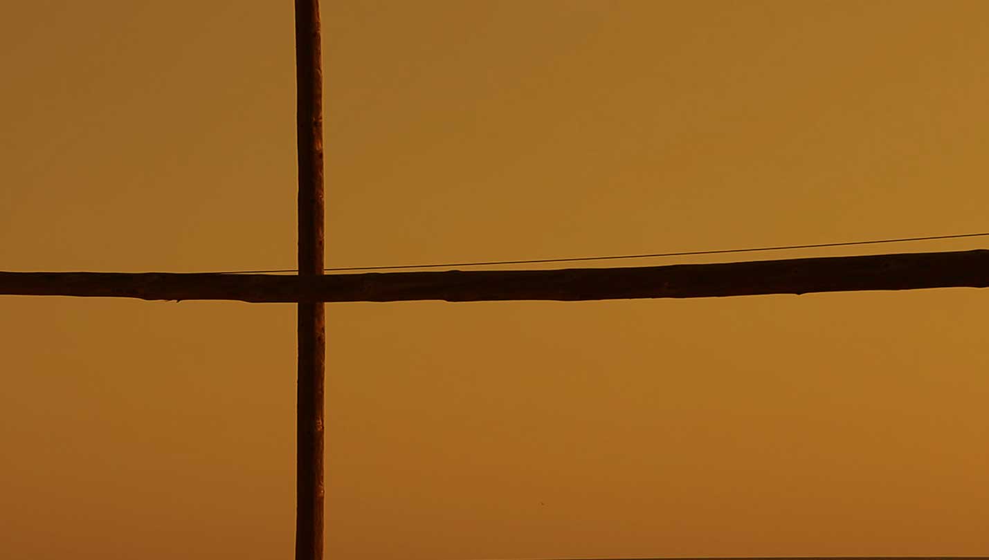 Poste de madera en cruz sobre un cielo anaranjado del atardecer.