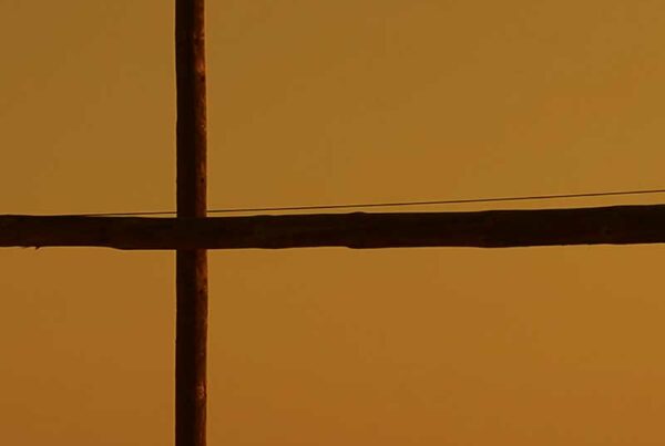 Poste de madera en cruz sobre un cielo anaranjado del atardecer.