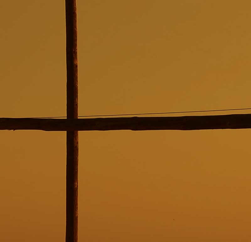 Poste de madera en cruz sobre un cielo anaranjado del atardecer.