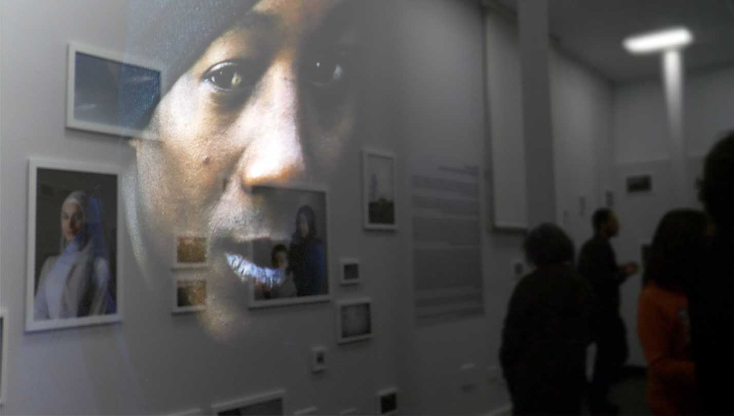Reflejo de la fotografía de un hombre en el cristal de una galería sobre el resto de obras de la exposición. Creando el efecto en el que una fotografía de una mujer en la pared y la imagen del reflejo en el cristal se miran entre sí.