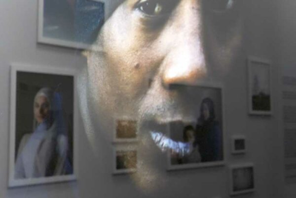 Reflejo de la fotografía de un hombre en el cristal de una galería sobre el resto de obras de la exposición. Creando el efecto en el que una fotografía de una mujer en la pared y la imagen del reflejo en el cristal se miran entre sí.