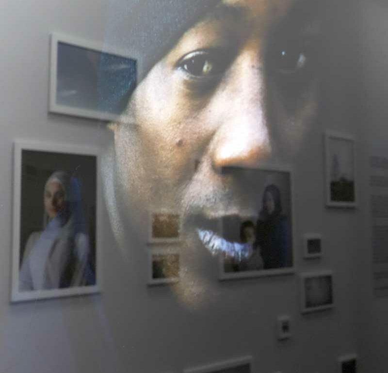Reflejo de la fotografía de un hombre en el cristal de una galería sobre el resto de obras de la exposición. Creando el efecto en el que una fotografía de una mujer en la pared y la imagen del reflejo en el cristal se miran entre sí.
