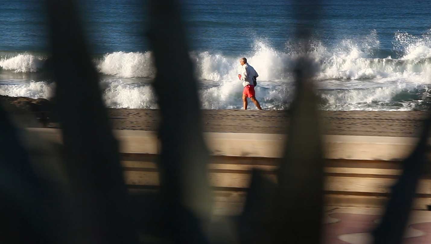 Hombre caminando por la orilla de la playa con el mar revuelto.